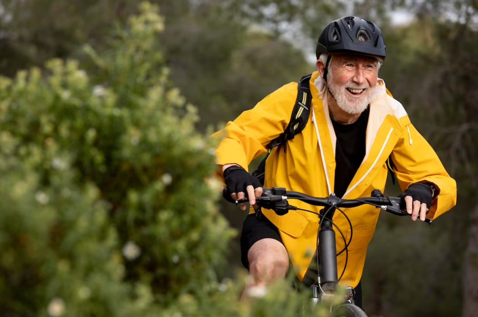 man in yellow jacket in helmet ride a bike , trees and bushes around him