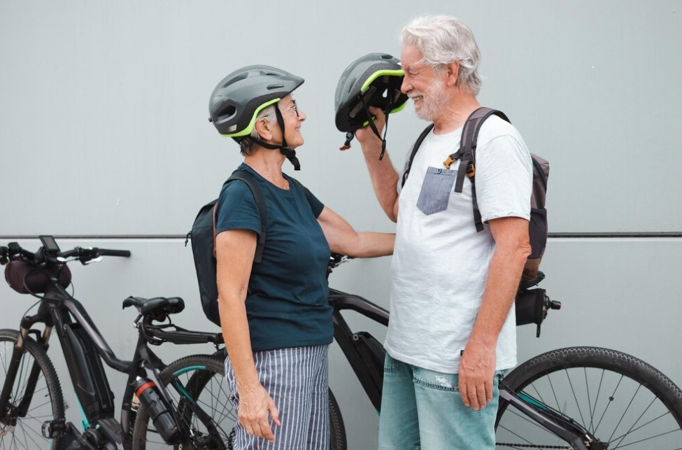 couple of pensioners standing in font of each other, woman in helmet, man holds the helmet near bikes