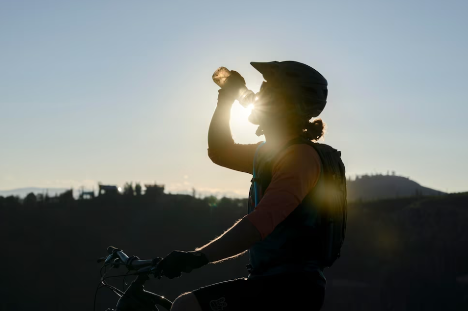 man drinks from a bottle of water, sunshine and city landscape behind him