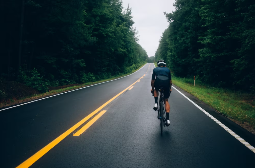 man in shorts riding a bike in the green forest on the road with yellow strip