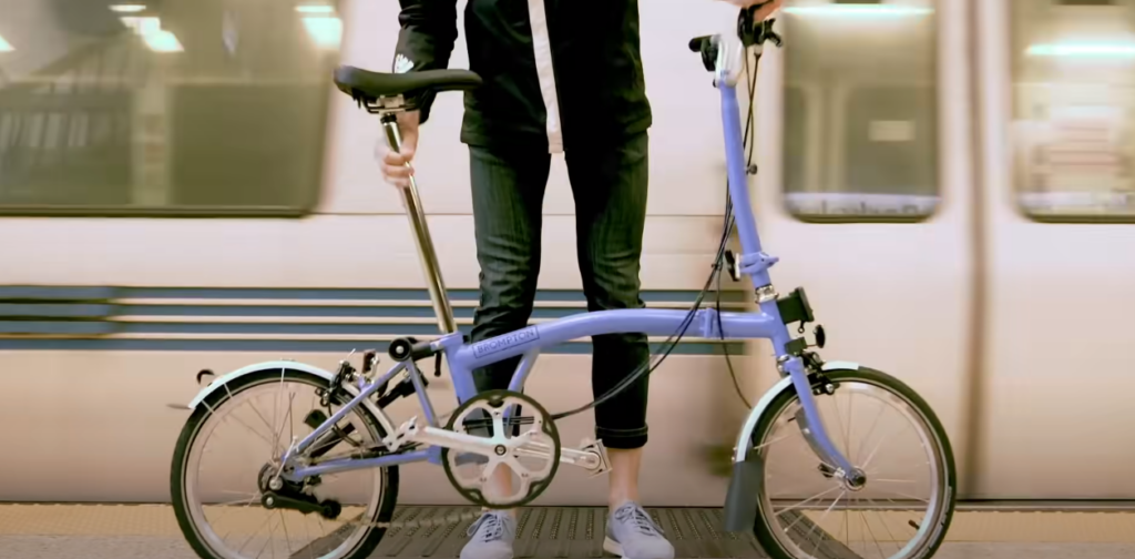 Hand holding a folding bike with a moving train in the background